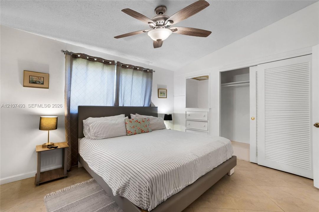 Main Apt West side, Bedroom, Neutral-toned tile flooring, ceiling fan with integrated lighting, built-in dresser with inset mirror, and sliding louvered closet doors