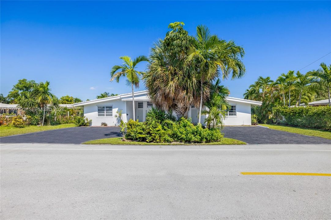 Single-story residence featuring a white exterior, expansive asphalt driveway, and mature landscaping