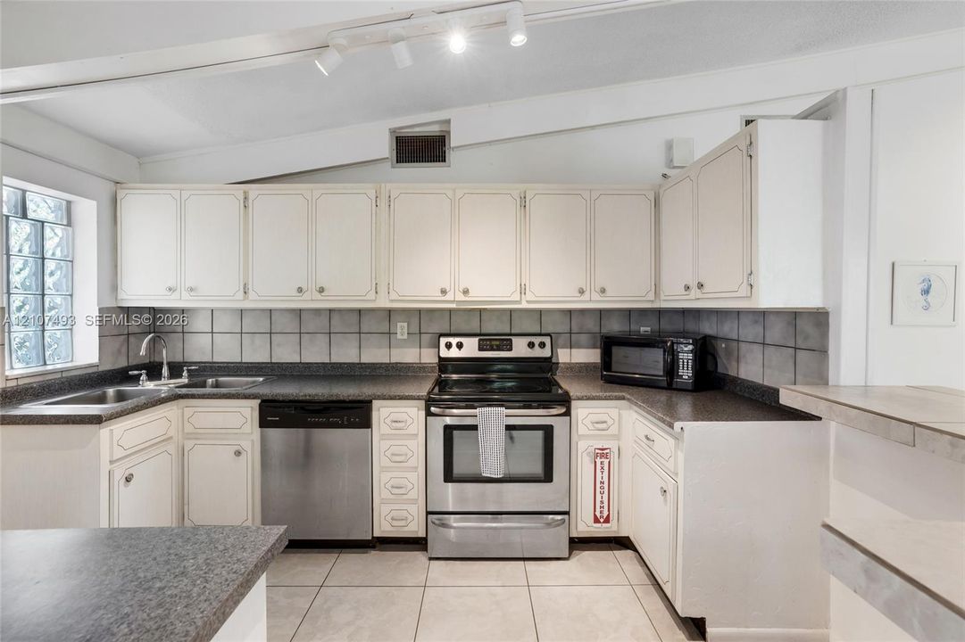 Main Apt, East side, Kitchen featuring cabinetry with white shaker-style doors, stone-finish countertops, stainless steel appliances, ceramic tile backsplash, and ceramic floor tiling