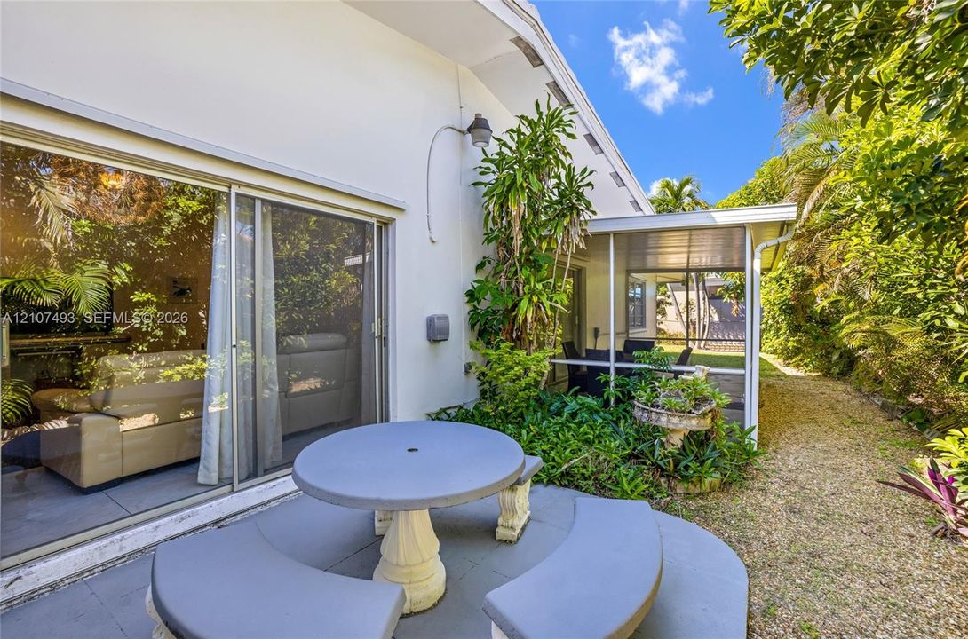 Main Apt, West side, Exterior patio featuring a concrete dining table with curved benches, sliding glass doors, and a screened-in lanai