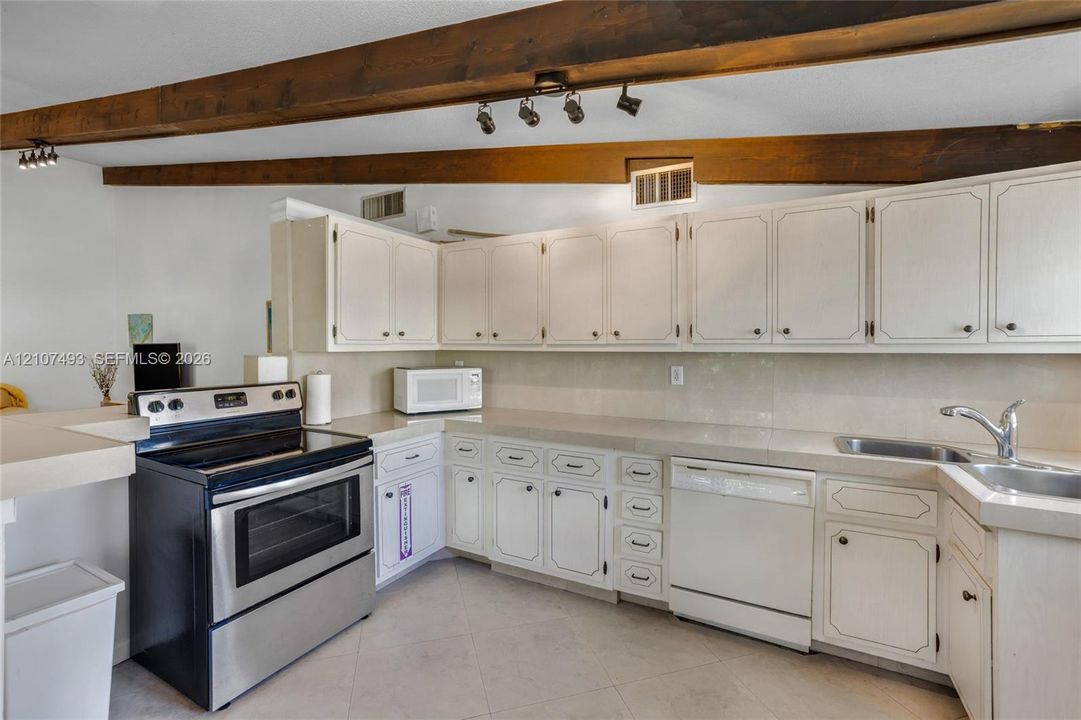 Main Apt, West side, Kitchen featuring white cabinetry, solid-surface countertops, stainless steel range, integrated dishwasher, and exposed wood ceiling beams