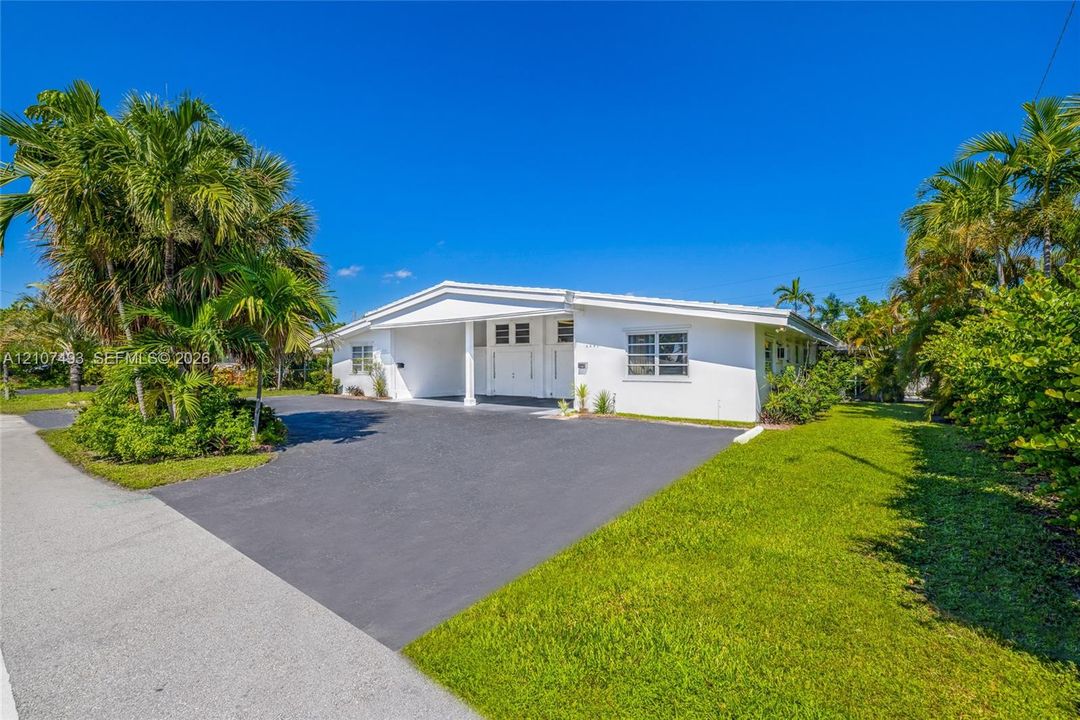 Front of Property, Single-story exterior featuring white stucco cladding, a paved driveway, a covered entrance, horizontal louvered windows, and mature palm trees