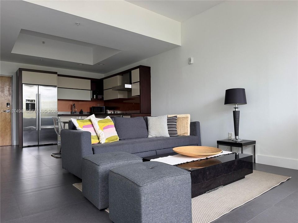 Open-concept area featuring oversized neutral floor tiling, recessed ceiling detail, and kitchen cabinetry with a two-tone finish
