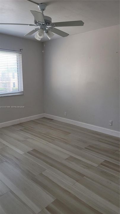 Interior space featuring wood-finish flooring, neutral wall paint, and a ceiling-mounted light fixture with a fan
