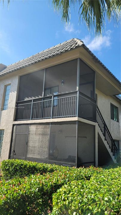 Two-story stucco exterior featuring stacked screened-in balconies, metal railings, and a tile roof