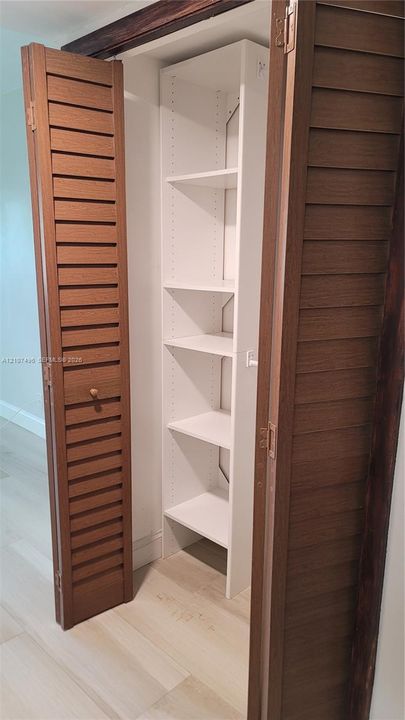 Storage closet featuring wood-finish louvered bi-fold doors and white custom built-in shelving