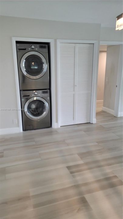 Stacked stainless steel laundry appliances and adjacent closet with white louvered doors, set against wood-finish flooring