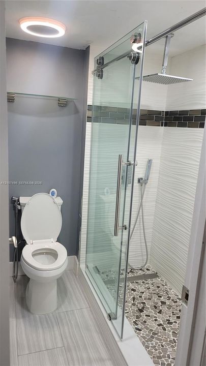Walk-in shower featuring a pebble-style tile floor, glass sliding door, square rain shower head, and textured wall tile