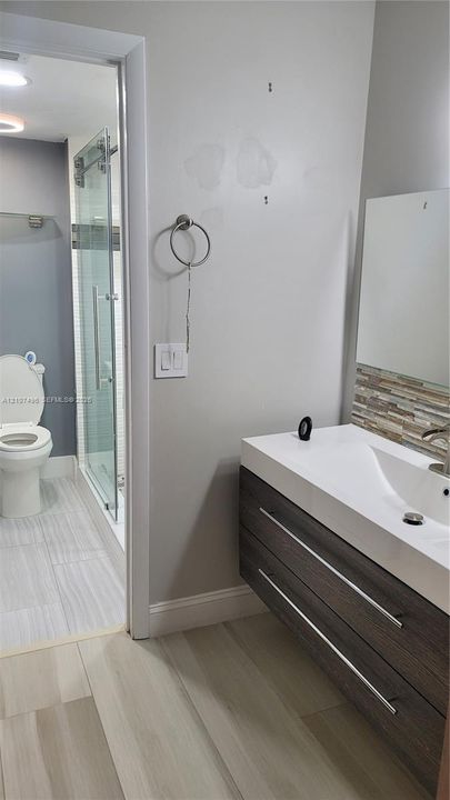 Floating vanity with dual soft-close drawers, integrated white basin, stacked stone backsplash, and wood-finish flooring