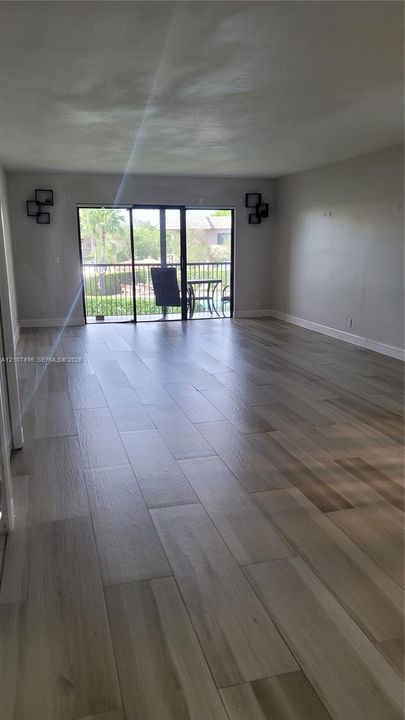 Open-concept living space featuring wood-finish flooring and sliding glass doors that provide access to a balcony with metal railing