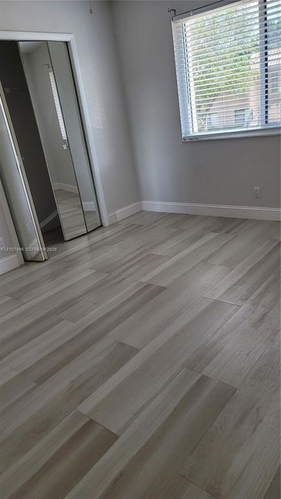 Neutral-toned wood-finish flooring, mirrored closet doors, and a window with horizontal blinds