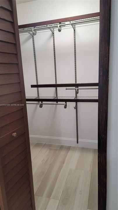Walk-in closet featuring wood-finish flooring, louvered doors, and multi-tier wire shelving with integrated hanging rods
