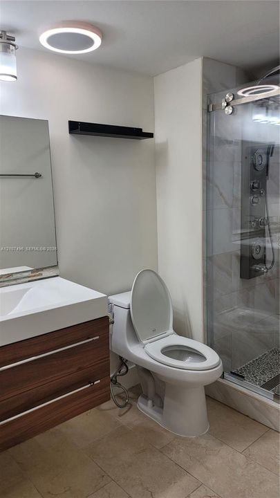 Modern floating vanity with a wood-finish cabinet and integrated sink, glass-enclosed shower featuring a multi-jet panel system, and light-toned floor tiling