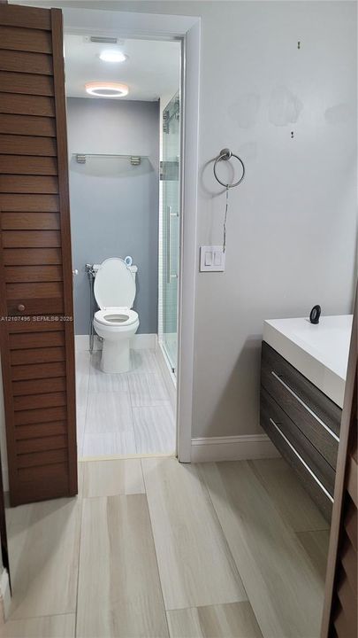 Modern floating vanity with a white countertop, wood-finish cabinetry, louvered closet doors, and large-format tile flooring