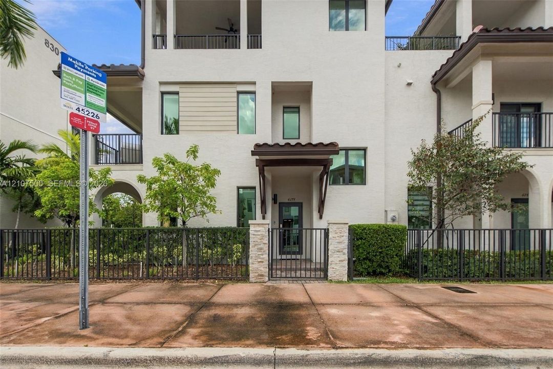 Stucco exterior featuring multi-level balconies, stone-accented entryway, tile roofing, and metal perimeter fencing
