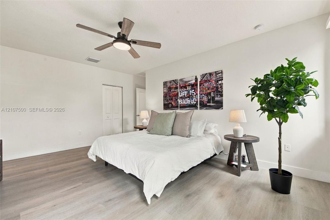 Neutral-toned room featuring wood-finish flooring, a multi-blade ceiling fan with integrated lighting, and white six-panel closet doors