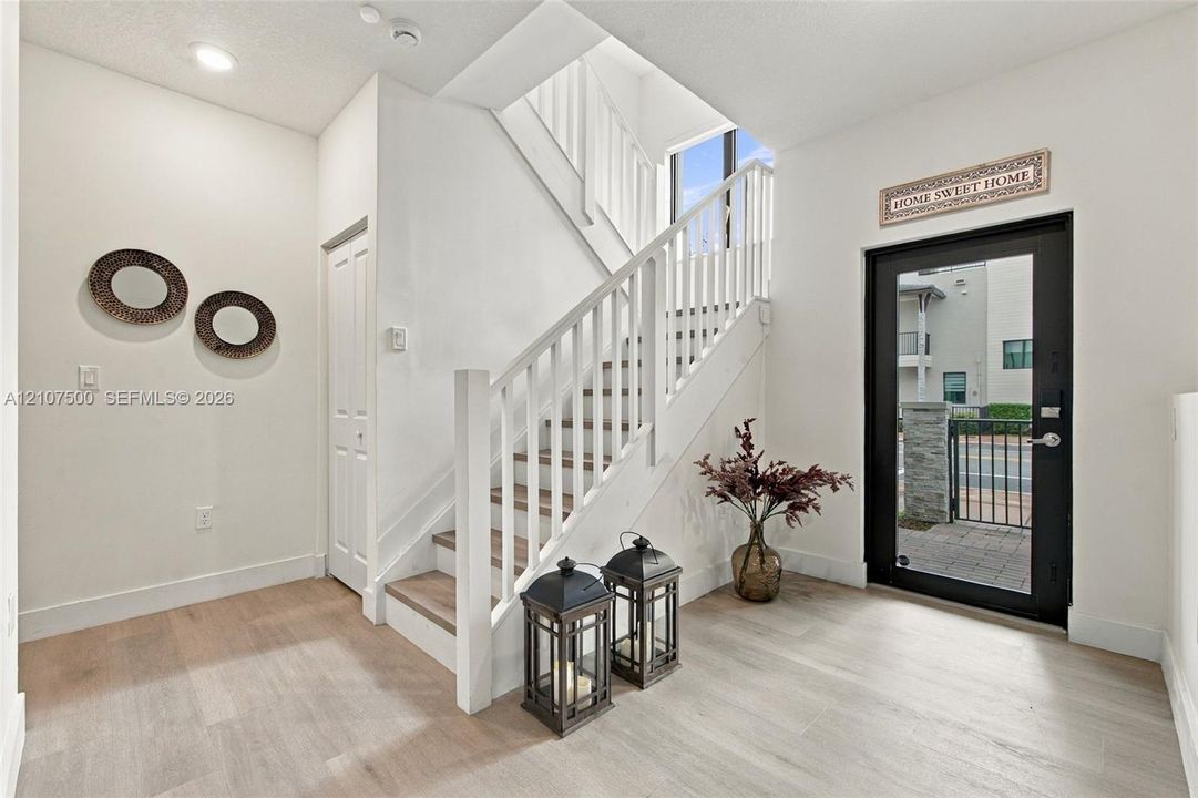 Foyer featuring wood-finish flooring, a glass-panel entry door, and a staircase with white painted balusters and wood-finish treads
