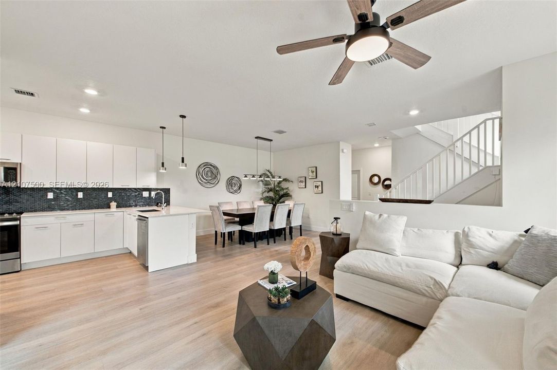 Kitchen featuring white flat-panel cabinetry, a dark tile backsplash, and a central island with countertop seating, complemented by wood-finish flooring, recessed lighting, and a modern ceiling fan