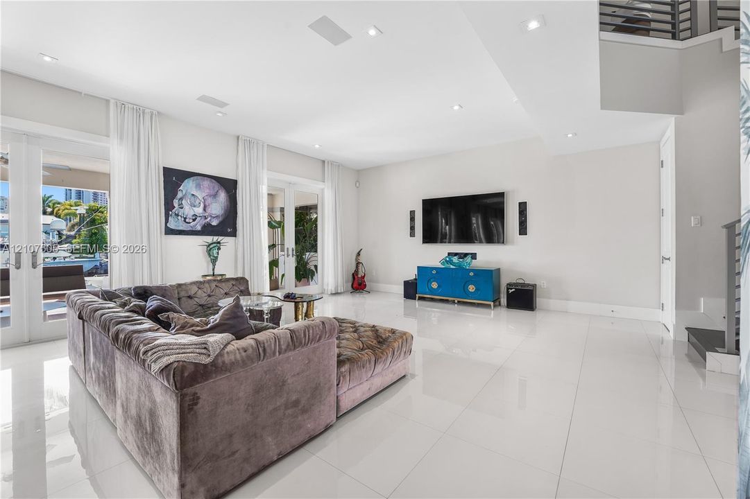 High-ceiling living area featuring large-format polished tile flooring, recessed lighting, and dual sets of glass-paneled double doors