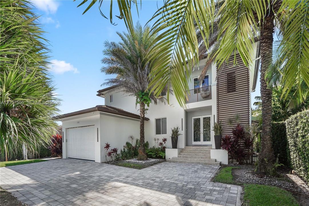 Two-story exterior featuring light-toned stucco, horizontal wood-slat accents, a paver driveway, an attached garage, and a covered front entry with stone-clad stairs