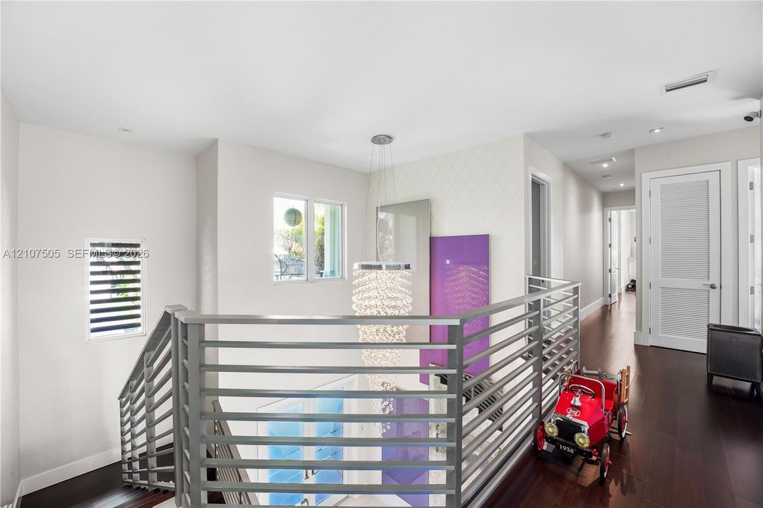 Landing area featuring dark wood-finish flooring, a tiered crystal chandelier, a metal horizontal-bar railing, and multi-panel interior doors