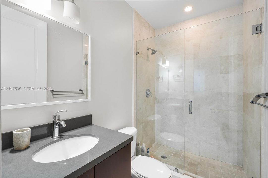 Bathroom featuring a stone-topped vanity with an undermount sink, a glass-enclosed shower with tile surround, and wall-mounted hardware