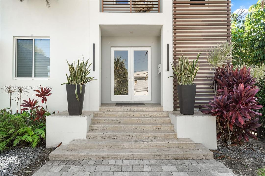 Modern architectural facade featuring a stone staircase entry, horizontal wood slat detailing, double glass-panel front doors, and vertical wall-mounted exterior lighting