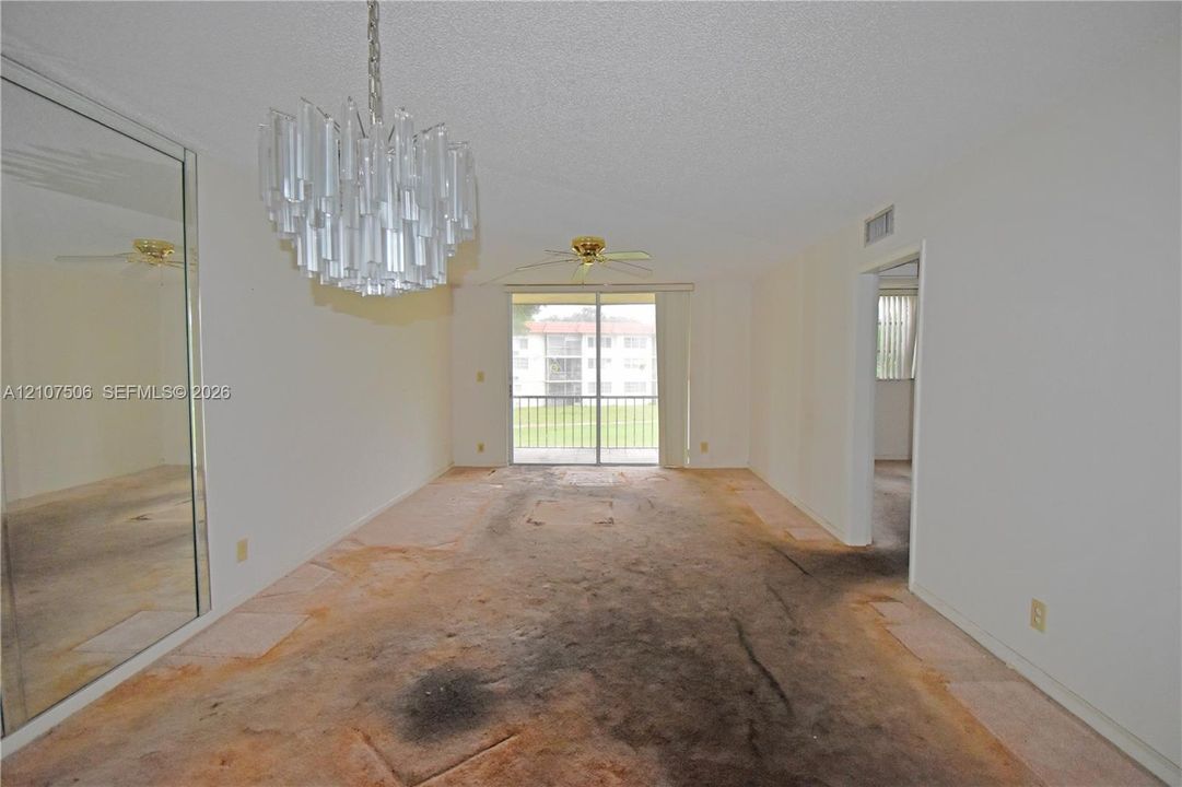 Living area featuring a tiered glass chandelier, mirrored wall paneling, a ceiling fan, and sliding glass doors leading to a balcony