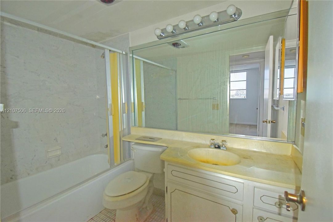 Full-width vanity with integrated countertop and sink, large wall-mounted mirror, overhead five-bulb vanity light, and tub-shower combination with surround