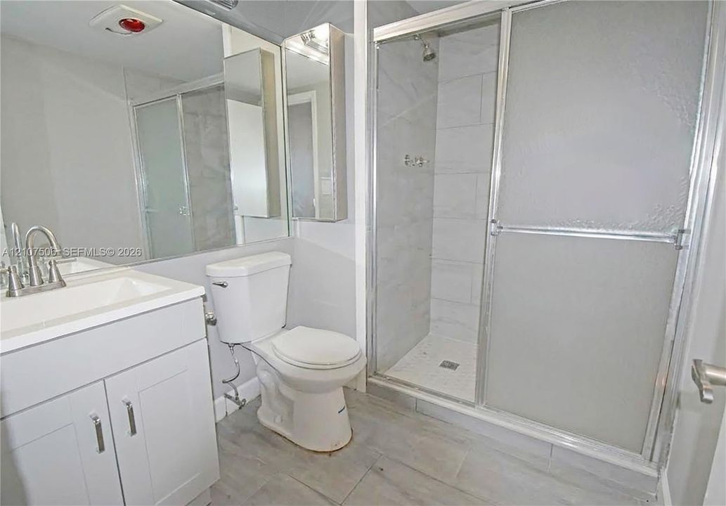 Bathroom featuring a white vanity cabinet, rectangular under-mount sink, tile-surround shower with sliding glass doors, and large-format tile flooring