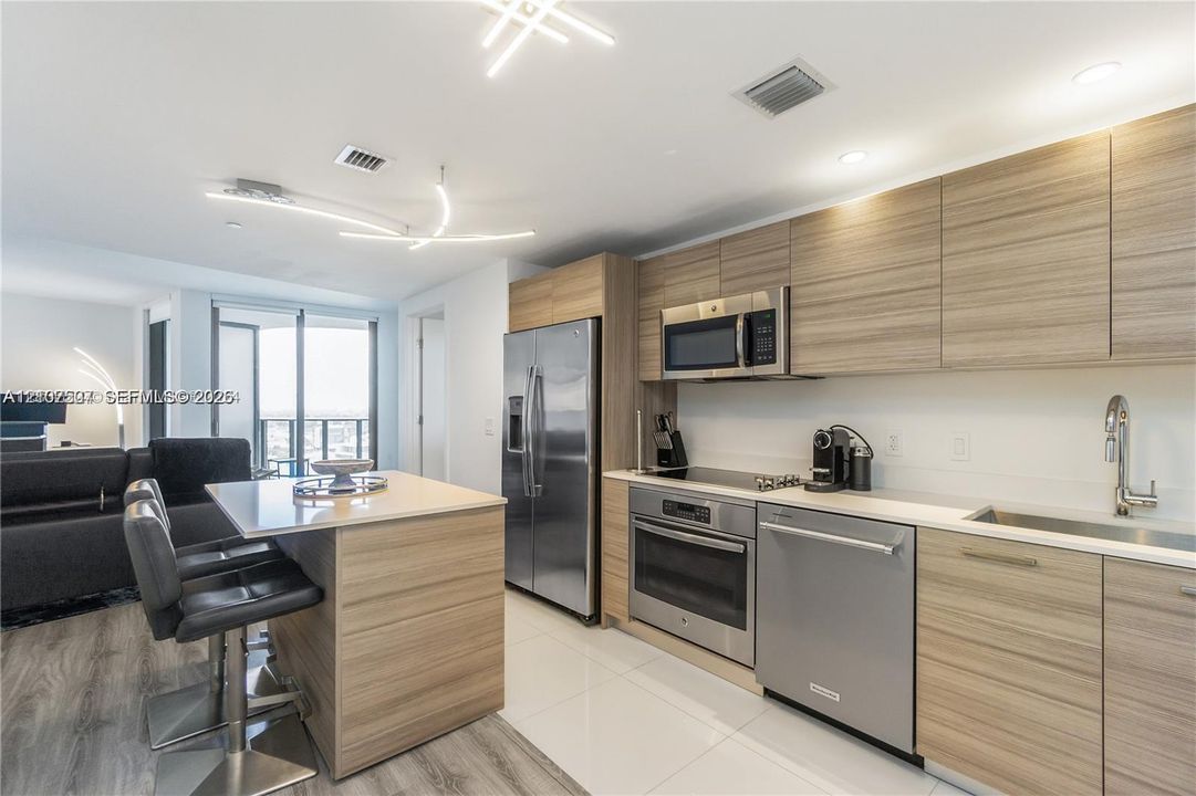 Modern kitchen featuring horizontal-grain wood-finish cabinetry, stainless steel appliances, quartz countertops, a matching island with integrated seating, and geometric LED lighting fixtures