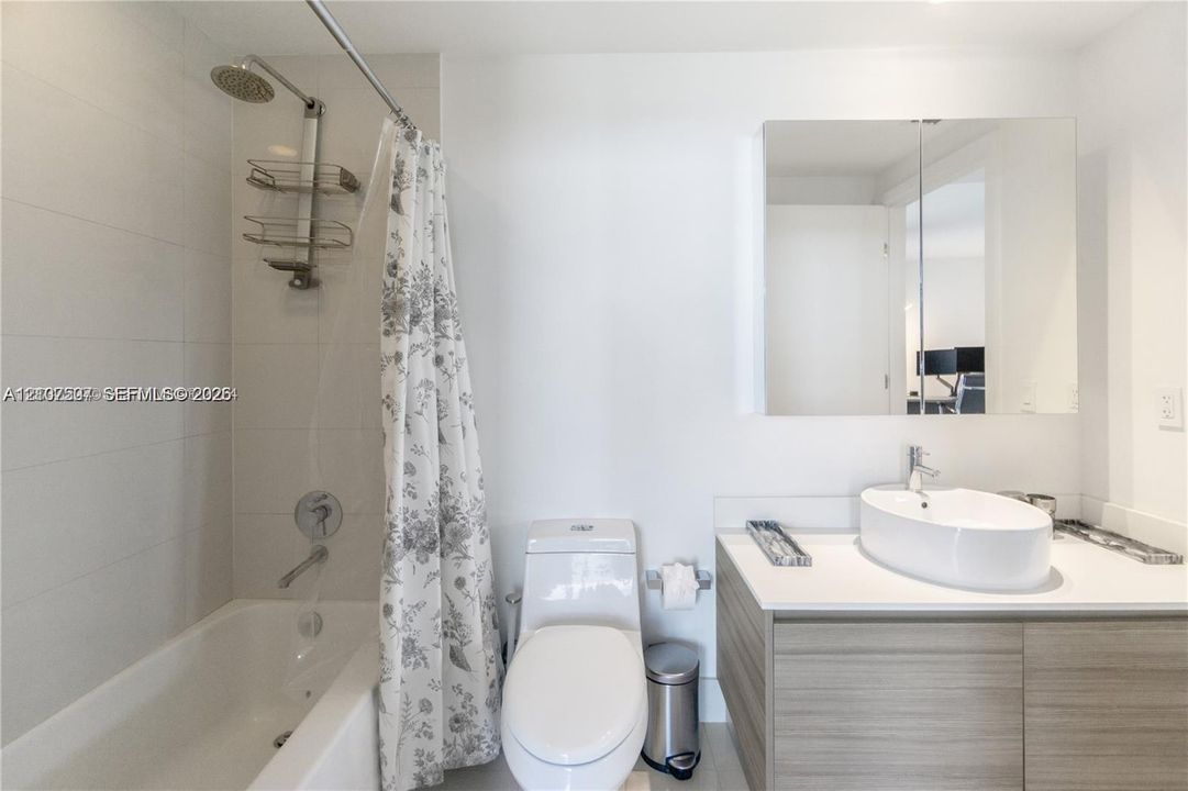 Bathroom featuring a wood-finish vanity with a white countertop and oval vessel sink, a mirrored medicine cabinet, and a tiled shower-tub combination with a wall-mounted shower head