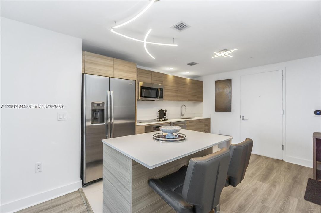 Kitchen featuring wood-finish cabinetry, a central island with a quartz countertop, stainless steel appliances, and contemporary linear light fixtures