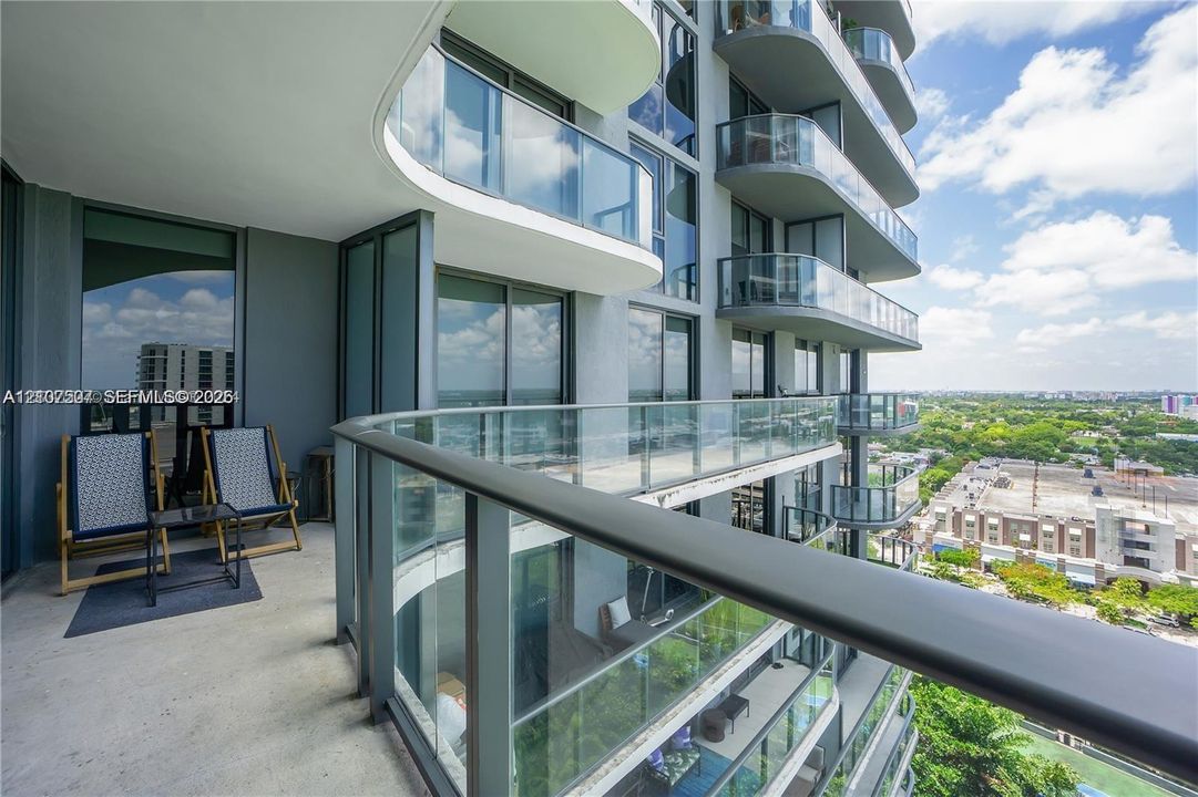 Covered balcony featuring a concrete floor, glass railings with dark-finish metal frames, and floor-to-ceiling sliding glass doors