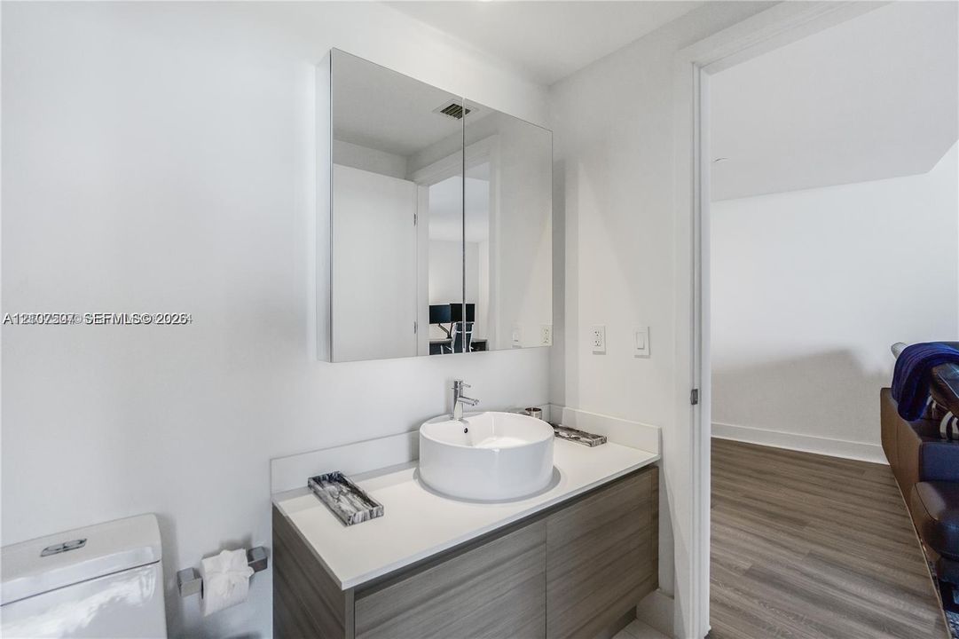Floating wood-finish vanity with a white vessel sink, polished chrome faucet, white countertop, and wall-mounted dual-door medicine cabinet