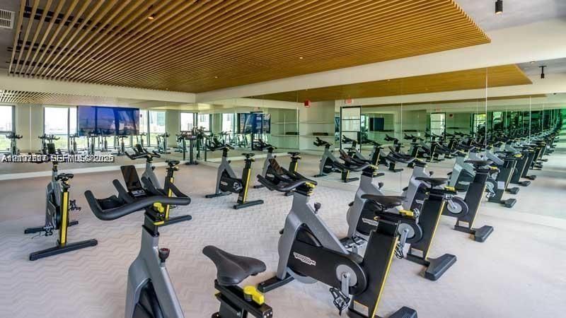 Fitness center featuring wood-slat ceiling detailing, floor-to-ceiling mirrors, large-format windows, and neutral patterned flooring