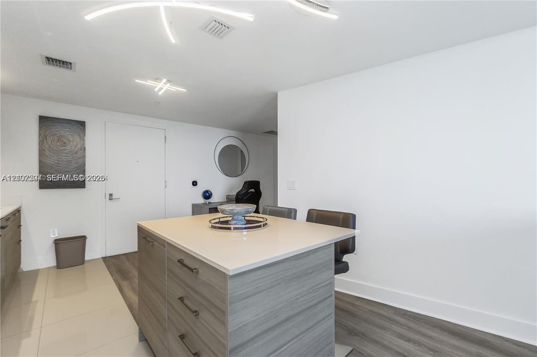 Center island featuring a light-toned countertop and wood-finish cabinetry with metal hardware, illuminated by modern geometric ceiling lighting