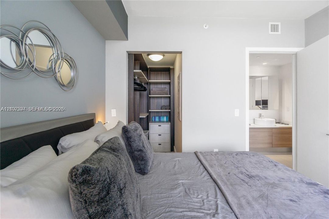 Custom walk-in closet with built-in shelving and drawers, wall-mounted floating wood-finish vanity, and integrated vessel sink