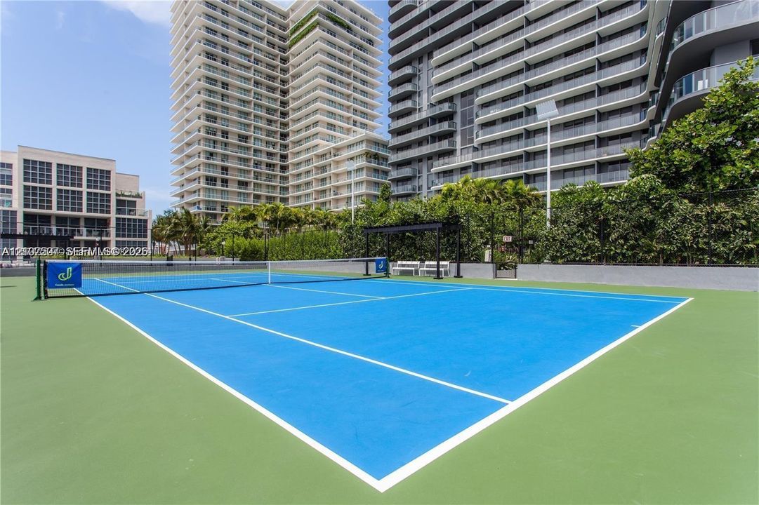 Tennis court featuring a blue playing surface, perimeter fencing, and overhead lighting