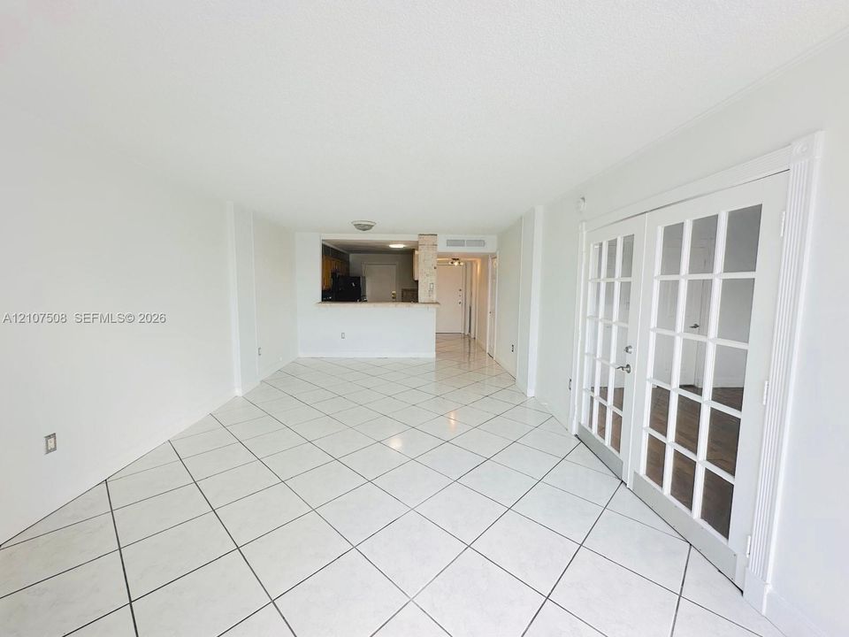 Large-format white tile flooring, French doors with glass panes, and a pass-through kitchen opening
