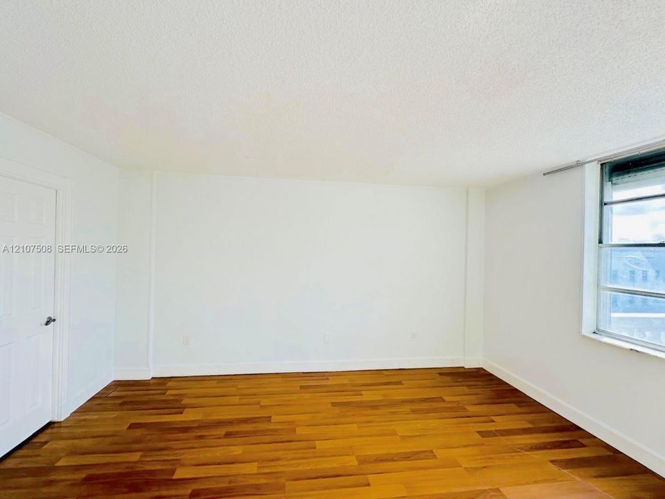 Room featuring wood-finish flooring, white walls, a six-panel door, and a single-pane aluminum window