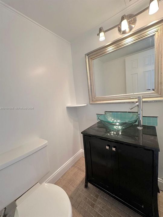 Black vanity cabinet with a stone countertop, circular glass vessel sink, chrome high-arc faucet, and a decorative tile backsplash