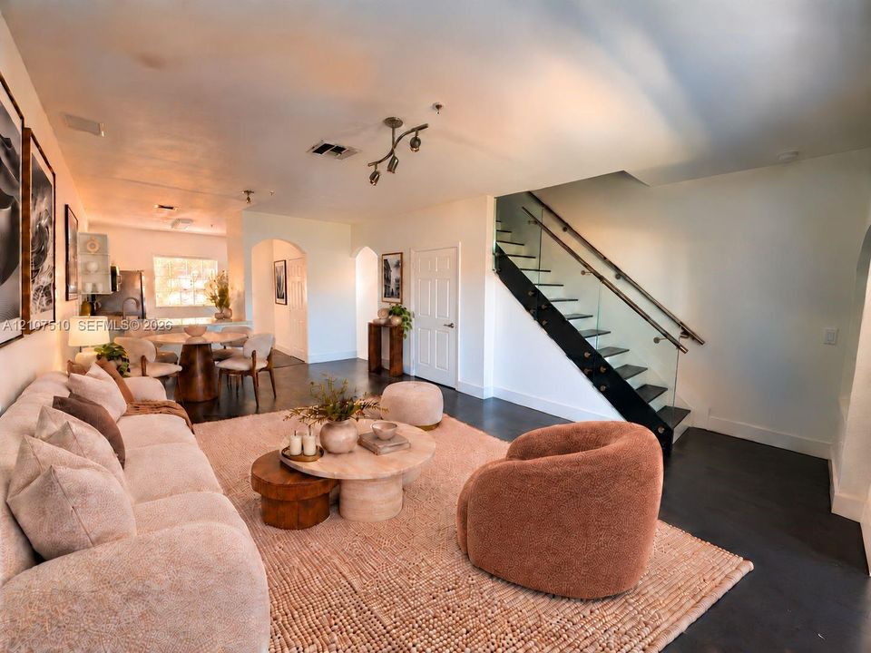 Open-concept interior featuring dark concrete flooring, arched doorways, and a staircase with a glass panel railing and metal handrail