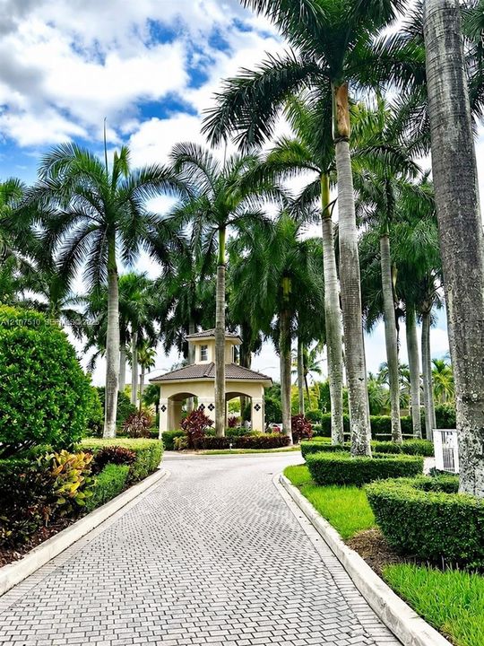 Paver stone driveway leading to a covered pavilion, surrounded by mature palm trees and manicured shrubbery