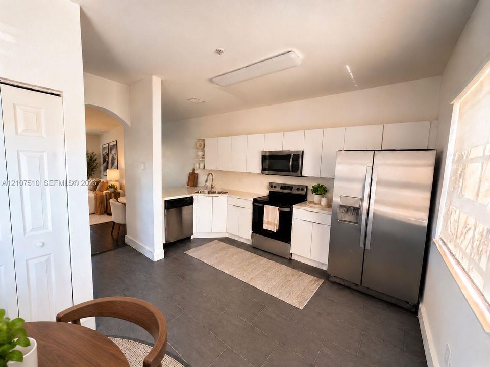 Kitchen featuring white flat-panel cabinetry, stainless steel appliances, solid-surface countertops, and dark tile flooring