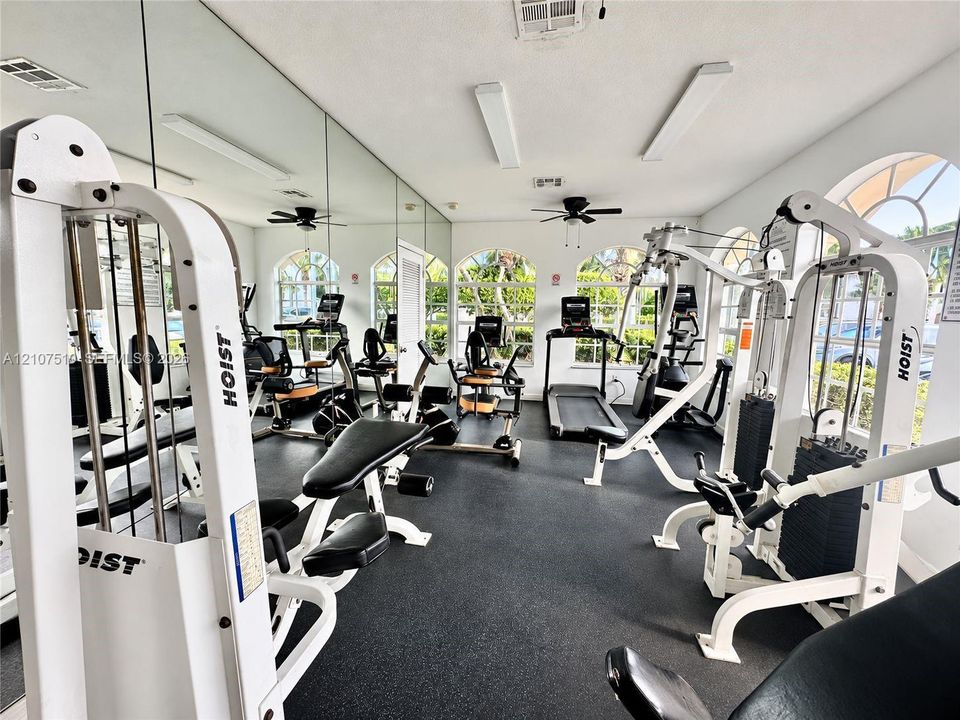 Fitness facility featuring rubberized flooring, floor-to-ceiling wall mirrors, arched windows, and integrated ceiling fans