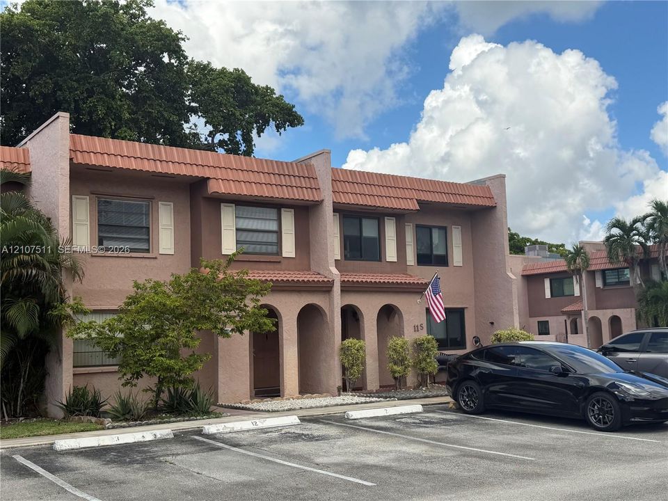 Two-story exterior featuring textured stucco facade, red tile roofing, arched entryways, and shuttered windows