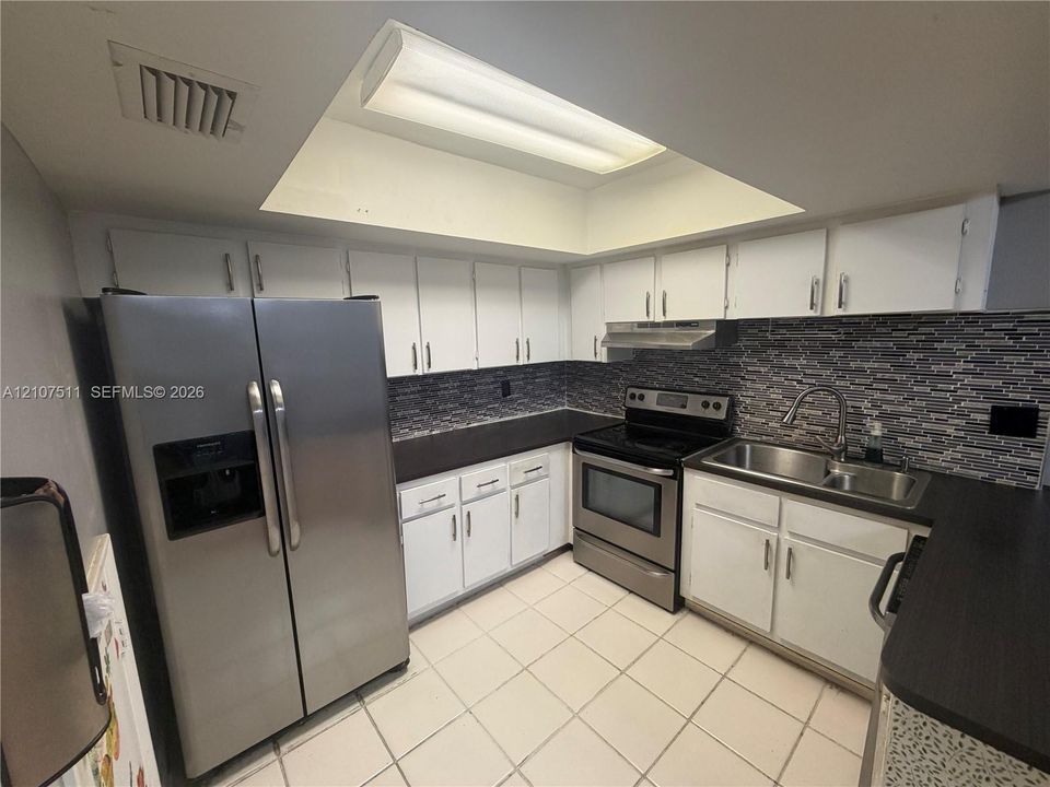 Kitchen featuring white cabinetry, stainless steel appliances, dark countertops, mosaic tile backsplash, and a recessed ceiling light fixture