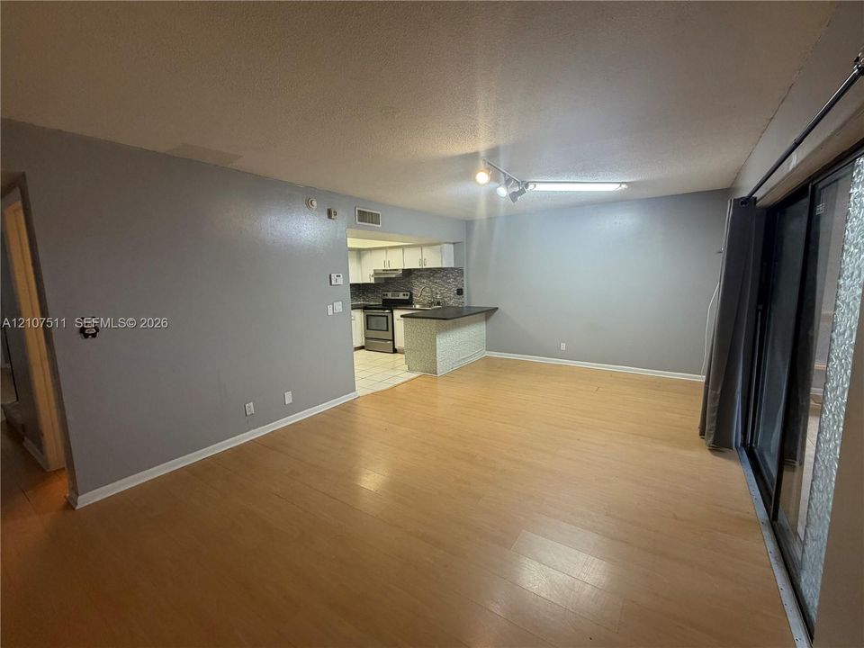 Open-concept living space featuring wood-finish flooring, a kitchen breakfast bar, and sliding glass patio doors