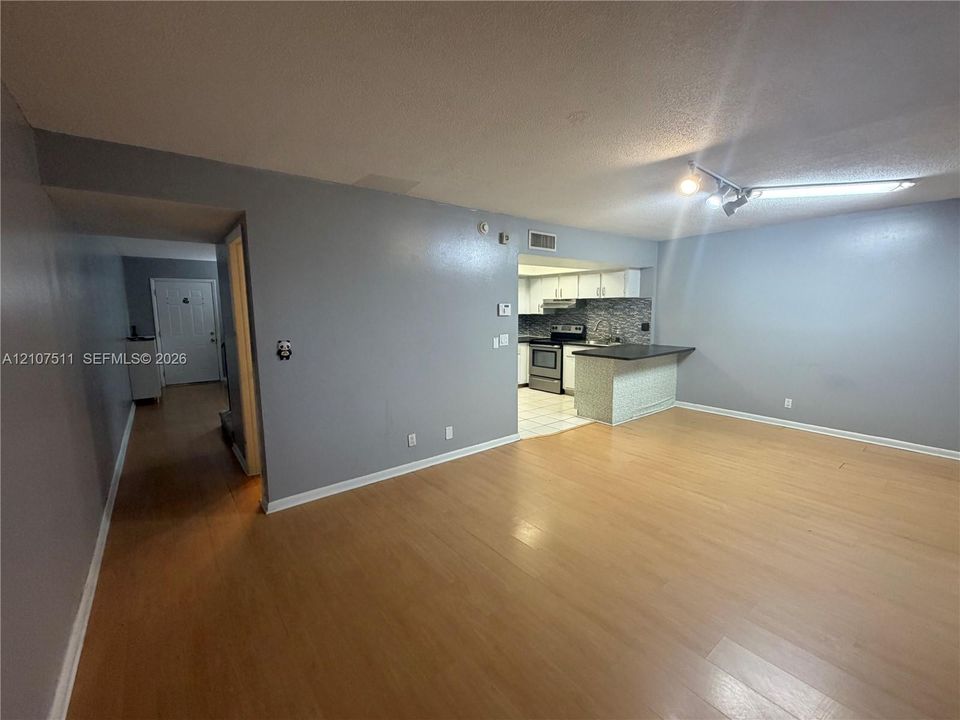 Open-concept interior featuring light wood-finish flooring, a kitchen breakfast bar with stone-finish base, tile flooring in the kitchen area, and track lighting